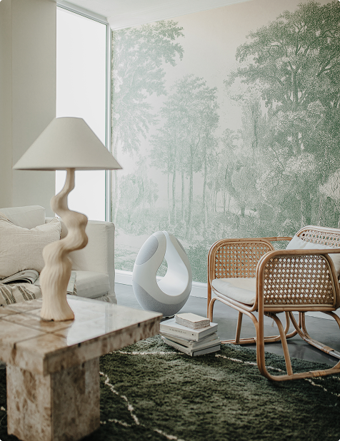 Pantheone I white audio sculpture styled in tranquil living room with rattan chairs and forest mural wallpaper