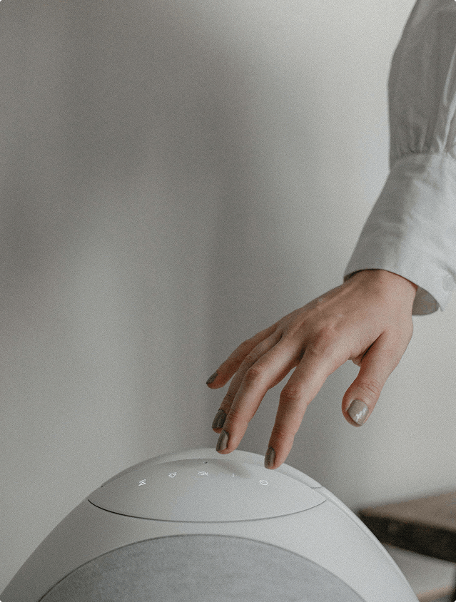A hand touching the top control panel of the Pantheone I wireless speaker