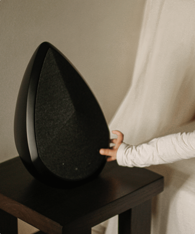 Child’s hand touching a black Pantheone Obsidian speaker on a dark wooden table.