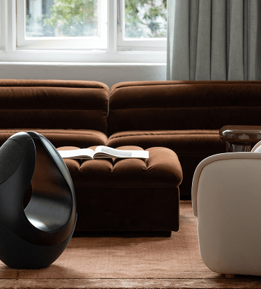 Pantheone I high-end wireless speaker in modern luxury interior beside tufted ottoman and soft lounge seating