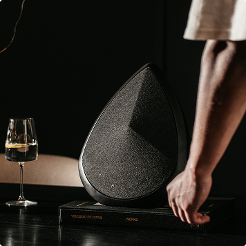 An obsidian Bluetooth speaker sitting on a cabinet next to a glass of wine 