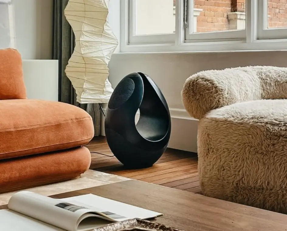 Black Pantheone I speaker next to a sofa and a chair.