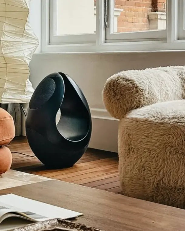 Black Pantheone I speaker next to a sofa and a chair.