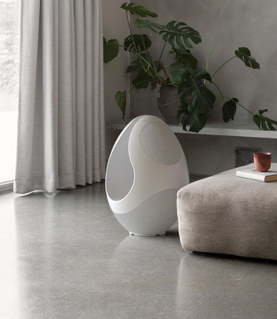 White Pantheone I speaker in a modern room with plants and a curtain.