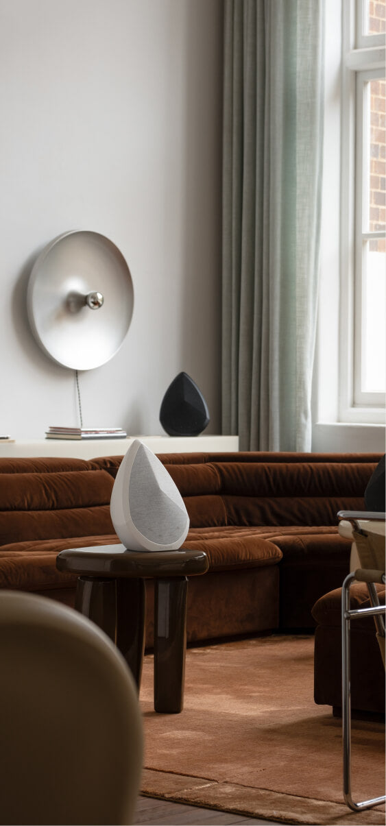 Pair of Pantheone Obsidian wireless speakers in white and black styled in a modern living room with velvet brown sofa and soft natural lighting
