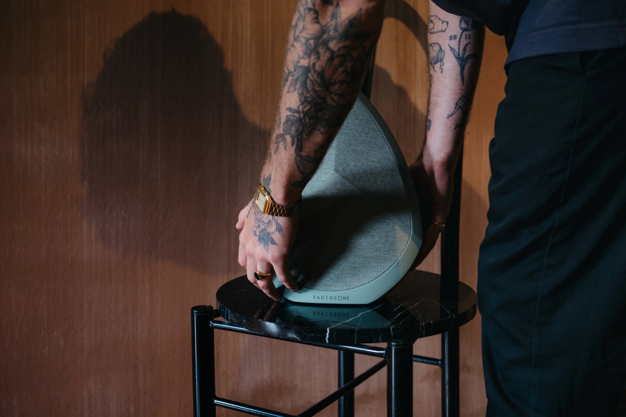 Person holding the Obsidian speaker on a black stool against a wooden wall.