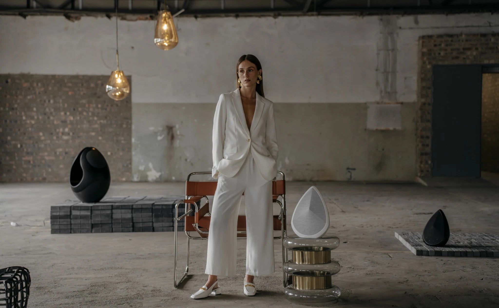A person in a white outfit standing in an industrial-style room with the Pantheone wireless speakers.