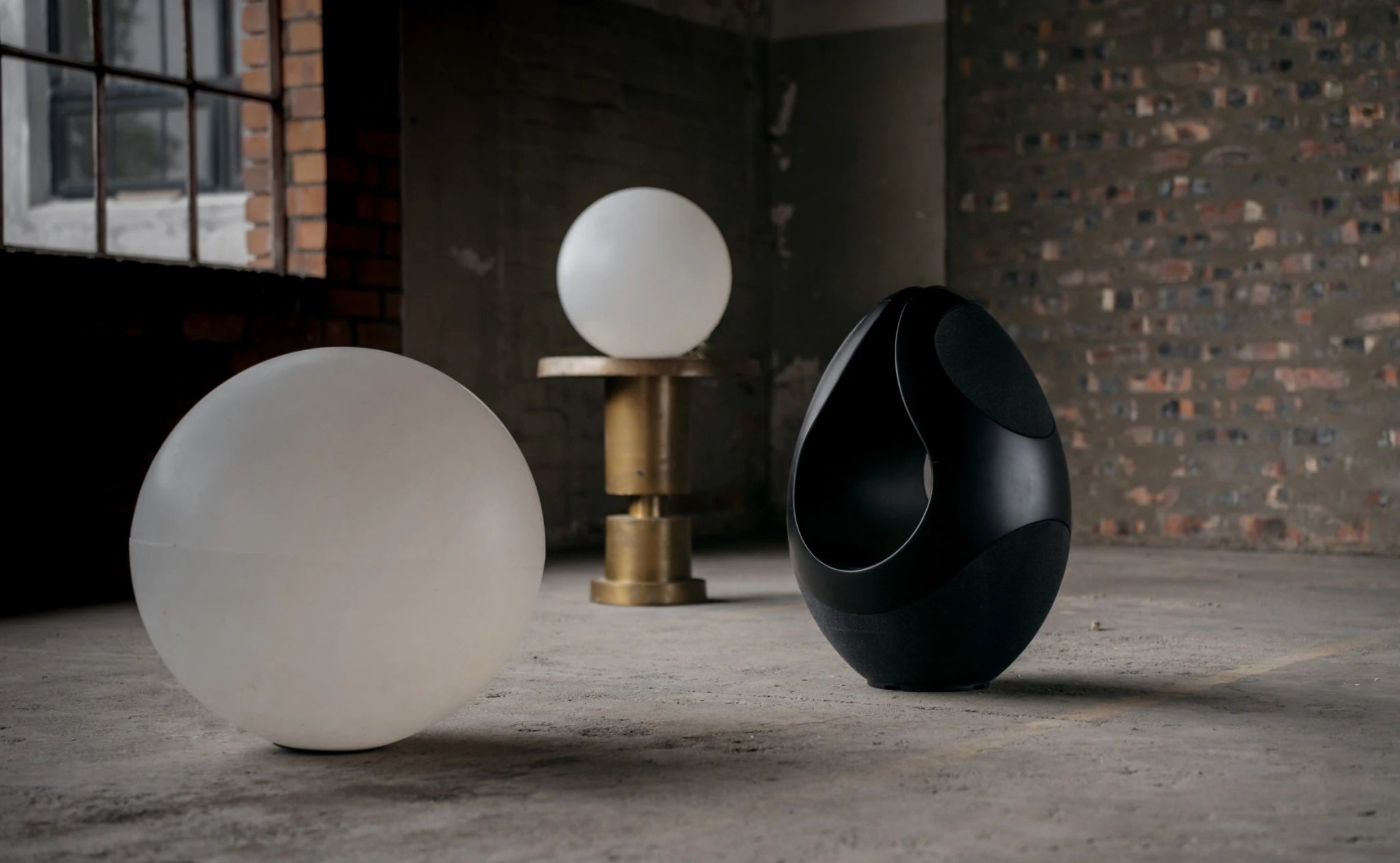 Pantheone I wireless speaker next to spherical objects on a concrete floor with a brick wall background