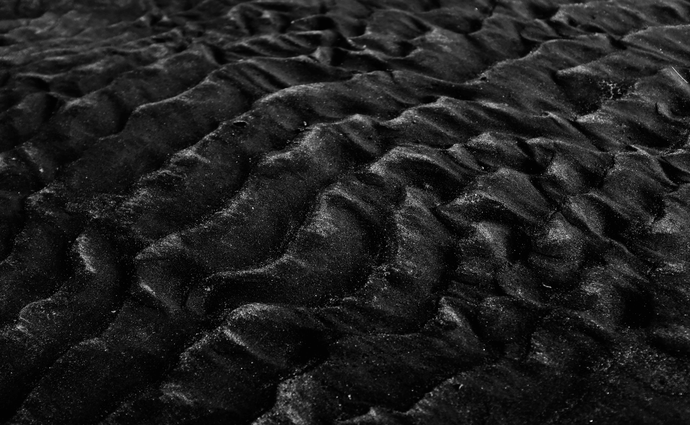 Close-up of rippled black sand with soft light and texture details.