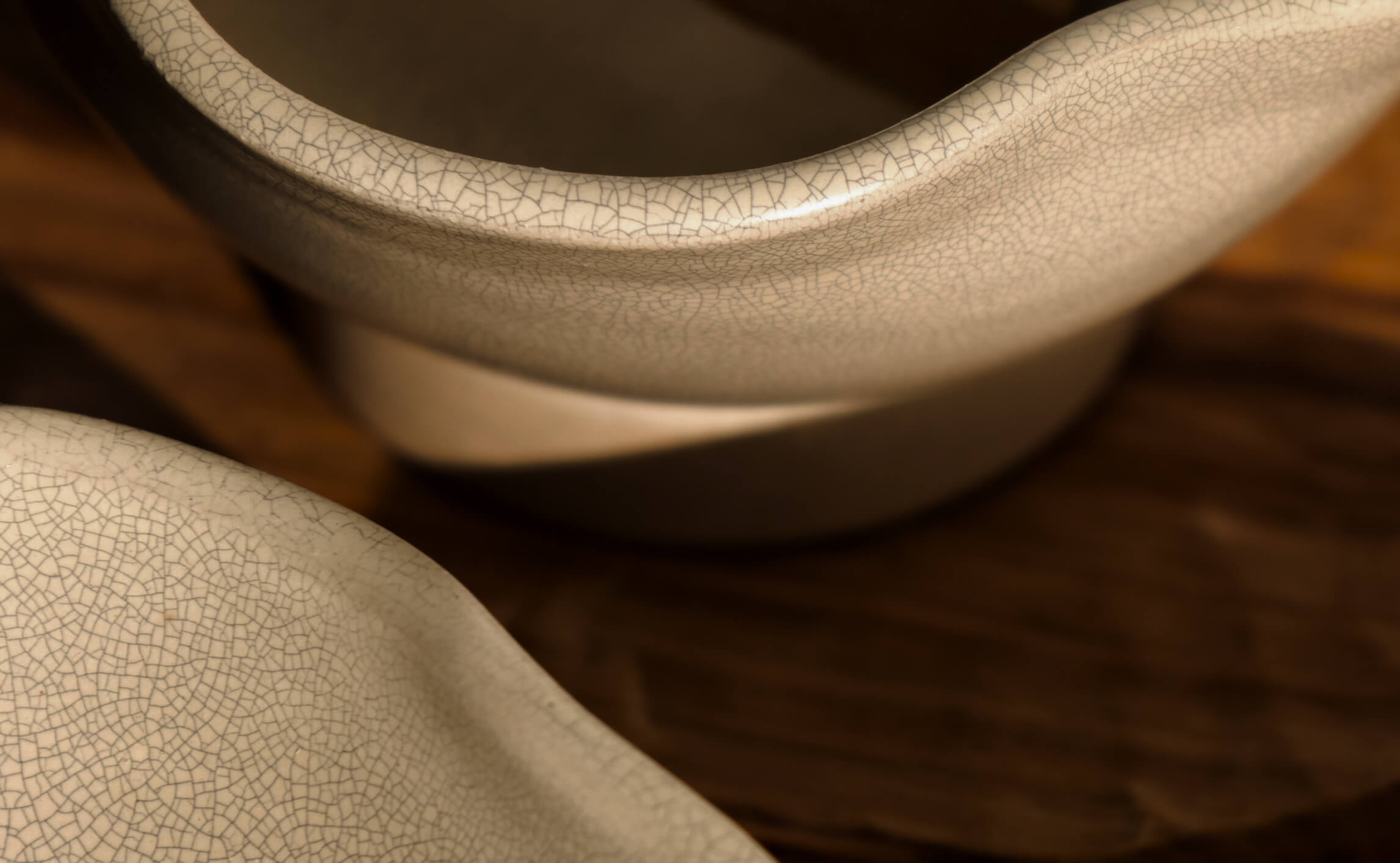 Close-up of ceramic bowls with a crackled glaze finish, resting on a wooden surface in warm light.