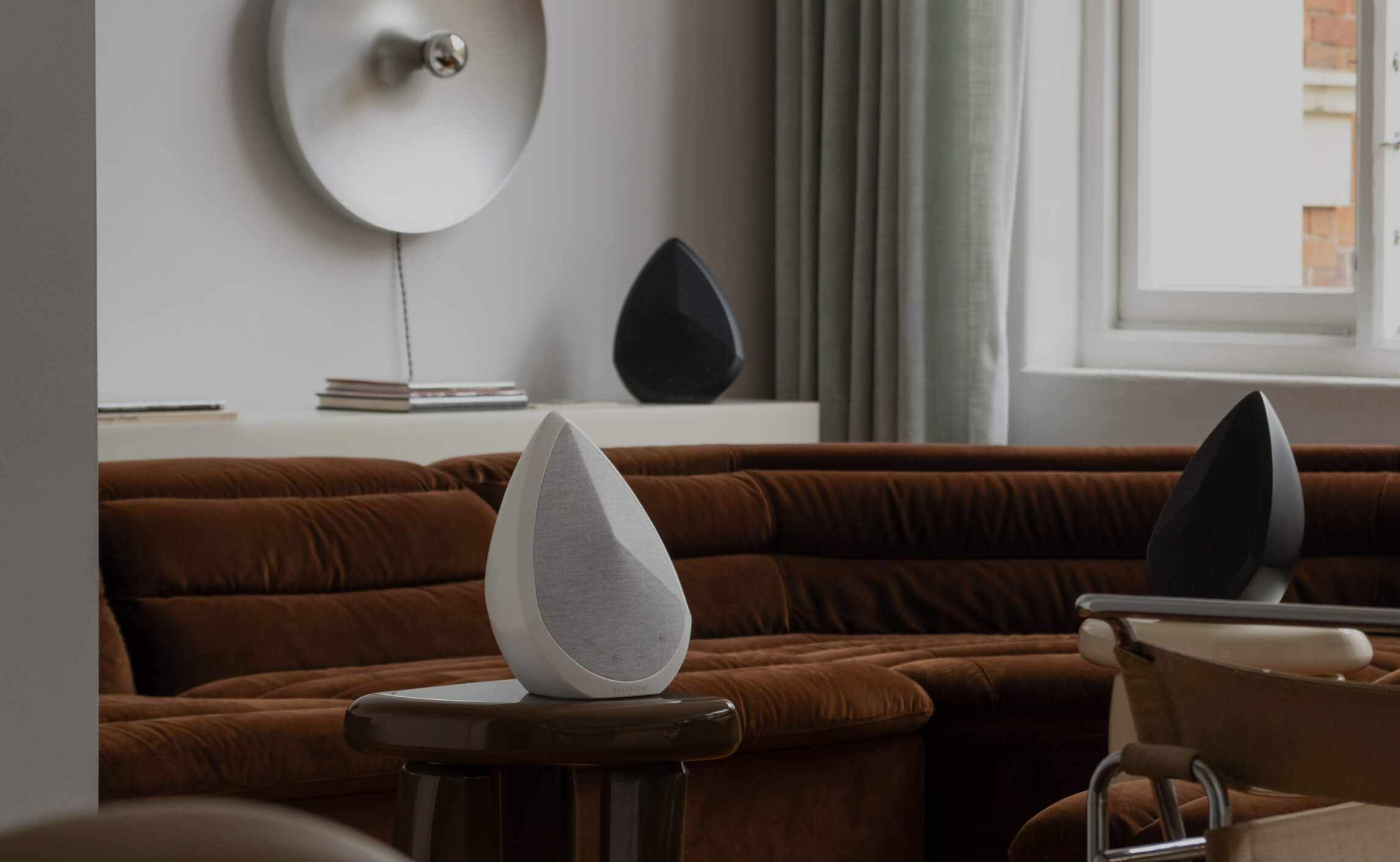 Pantheone Obsidian wireless speakers in white and black styled in a modern living room with velvet brown sofa and soft natural lighting