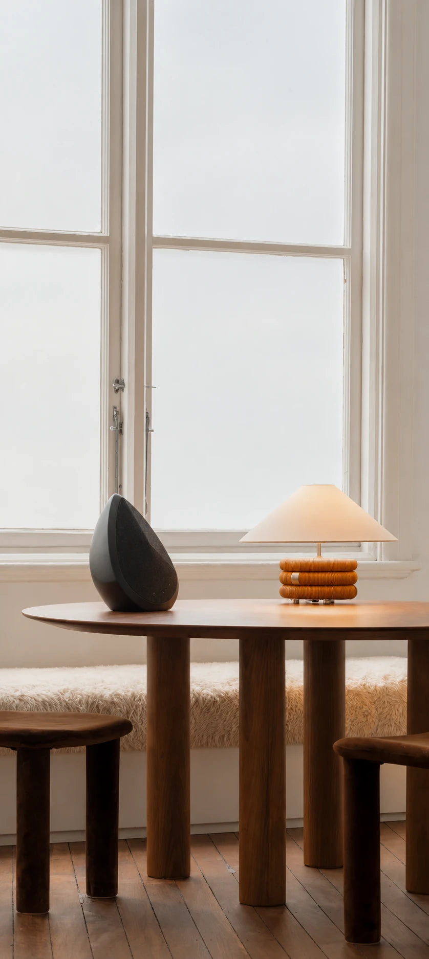 The Obsidian wireless peaker on a wooden table with a lamp and chair in a bright room
