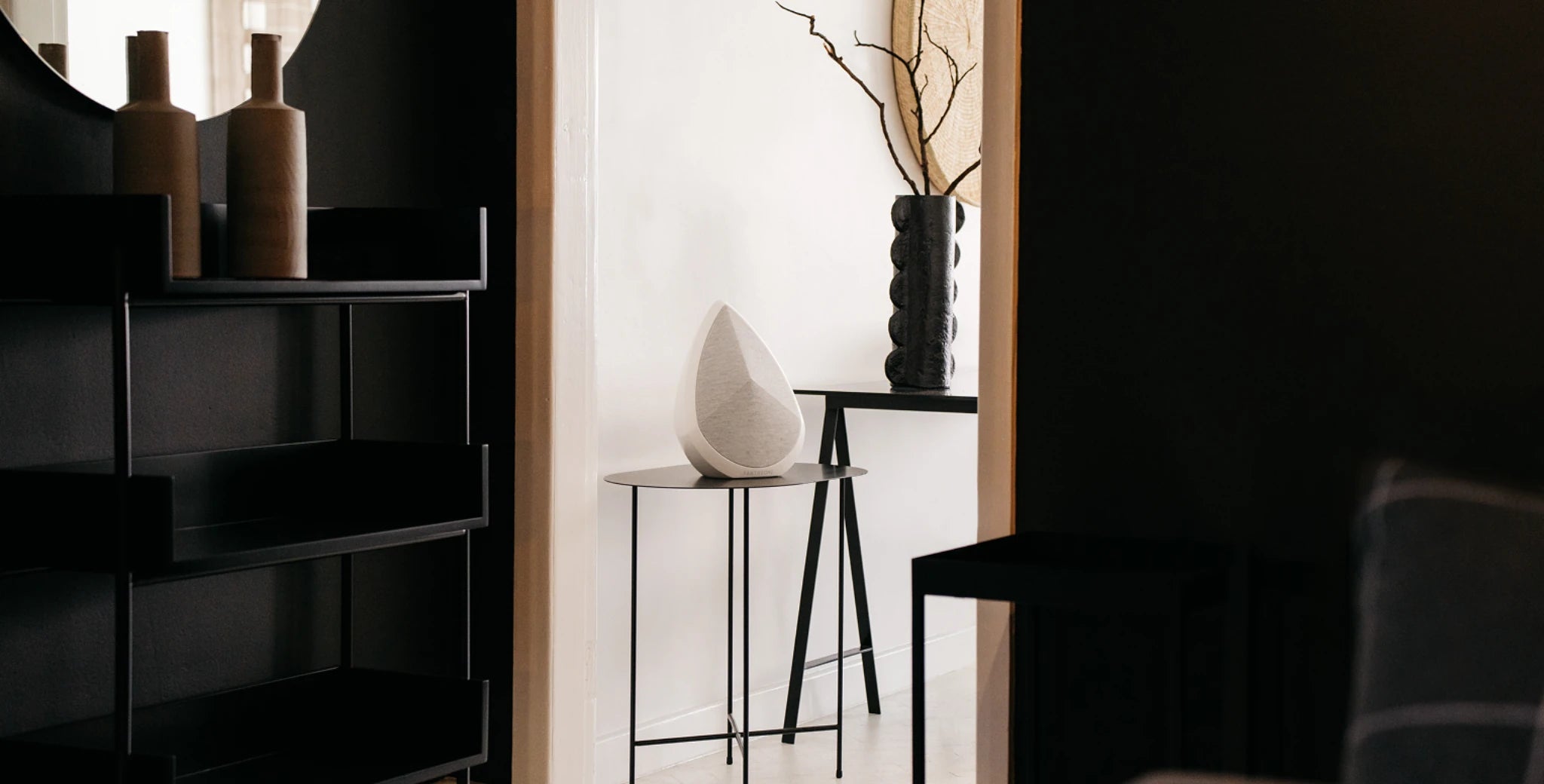 Modern interior with a black shelving unit, a white Obsidian speaker, and a black stool.