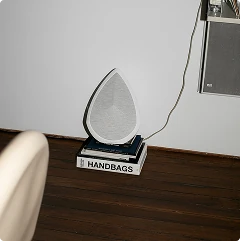 Obsidian portable speaker on a black base with 'HANDBAGS' text, placed on a wooden surface.