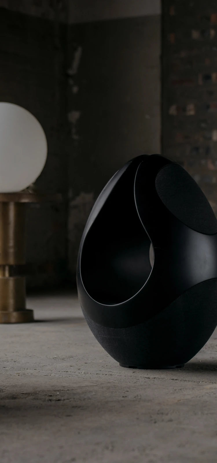 Pantheone I wireless speaker next to spherical objects on a concrete floor with a brick wall background