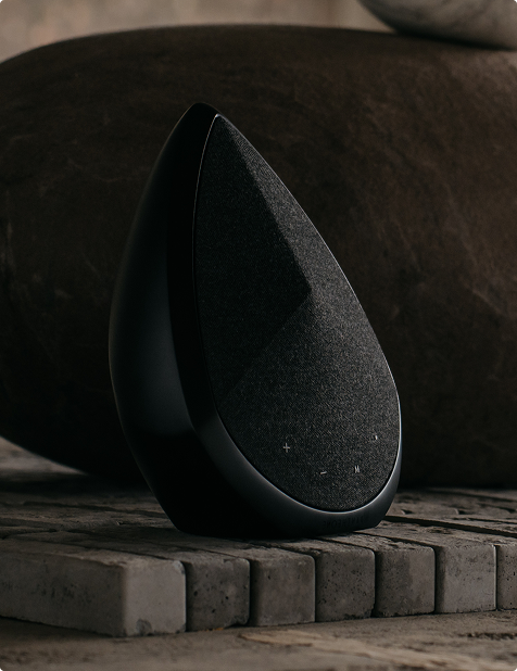 An obsidian portable wireless speaker is placed on bricks in an industrial room