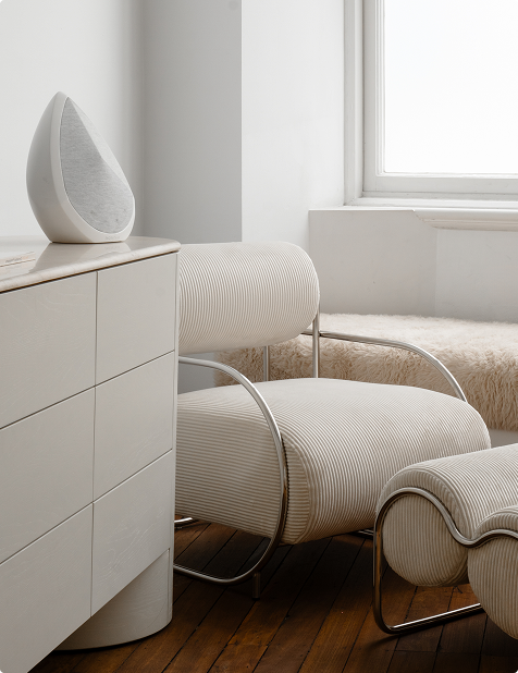 Obsidian wifi speaker styled on sculptural white side table beside modern white chair