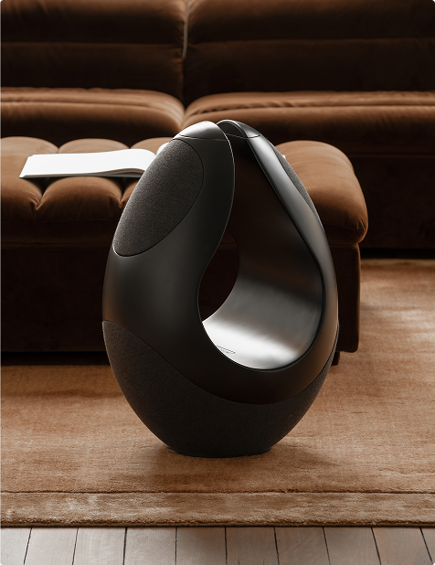 Pantheone I black wireless speaker placed in front of velvet ottoman with open book in designer living room