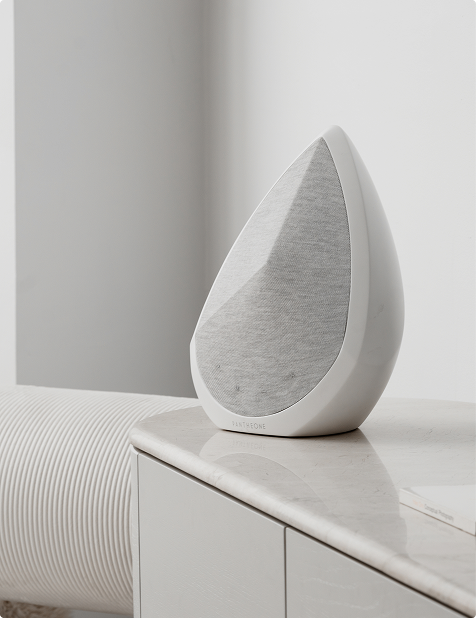 White Obsidian portable wireless speaker, a compact, rectangular speaker with rounded edges, in a bright light on a sculptural side table