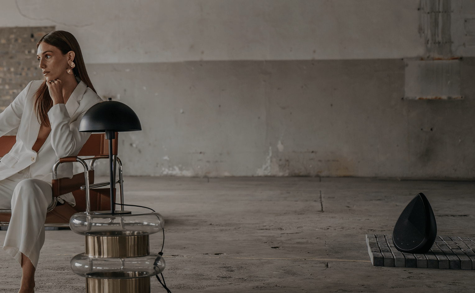 Obsidian Bluetooth speaker in an industrial space with a model sitting next to a stylish lamp 