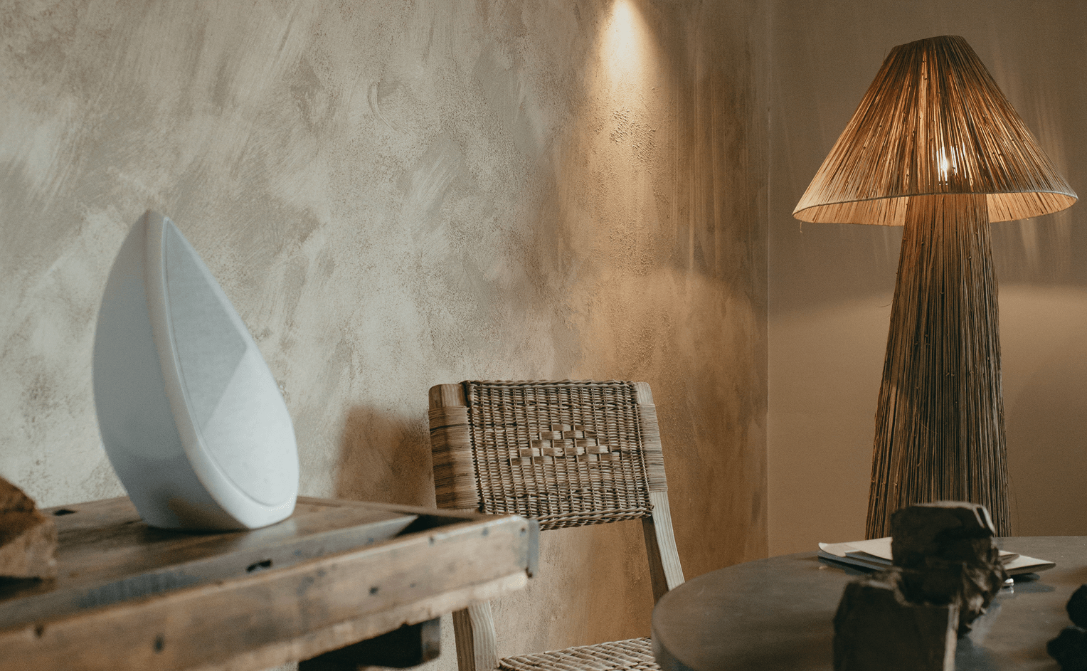 Obsidian white active speaker styled on rustic wooden table in minimalist natural toned interior with woven chair and sculptural floor lamp