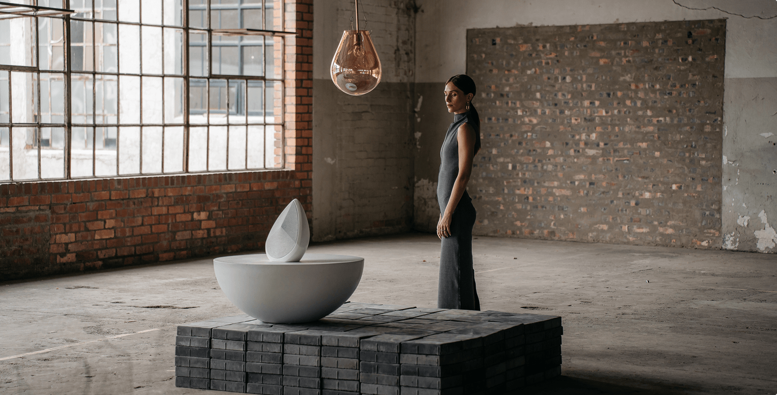 Woman in a minimalist loft standing beside a sculptural white Obsidian speaker.