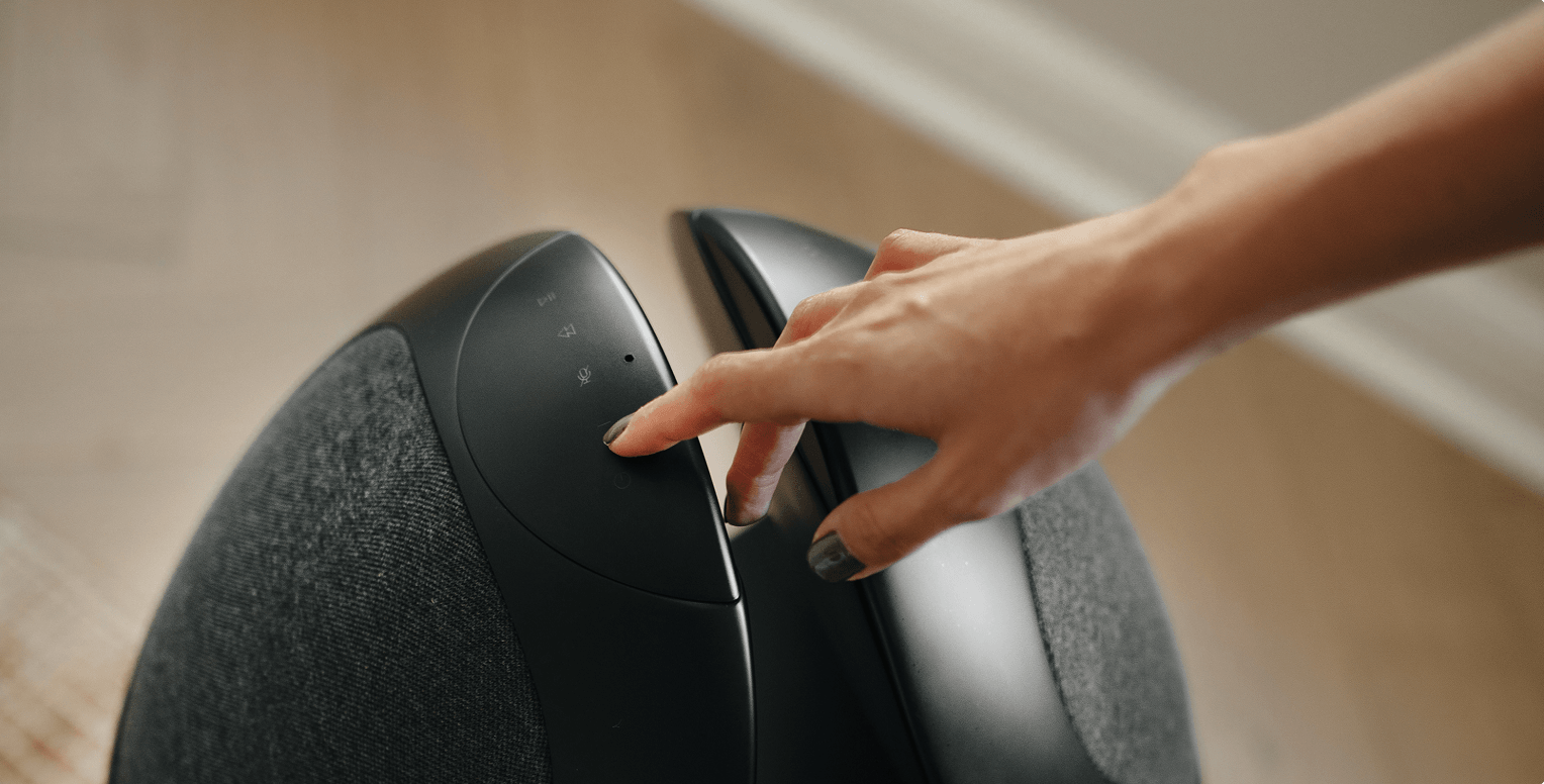 Hand gently touching the power button on a black Pantheone I 360 sound wireless speaker.