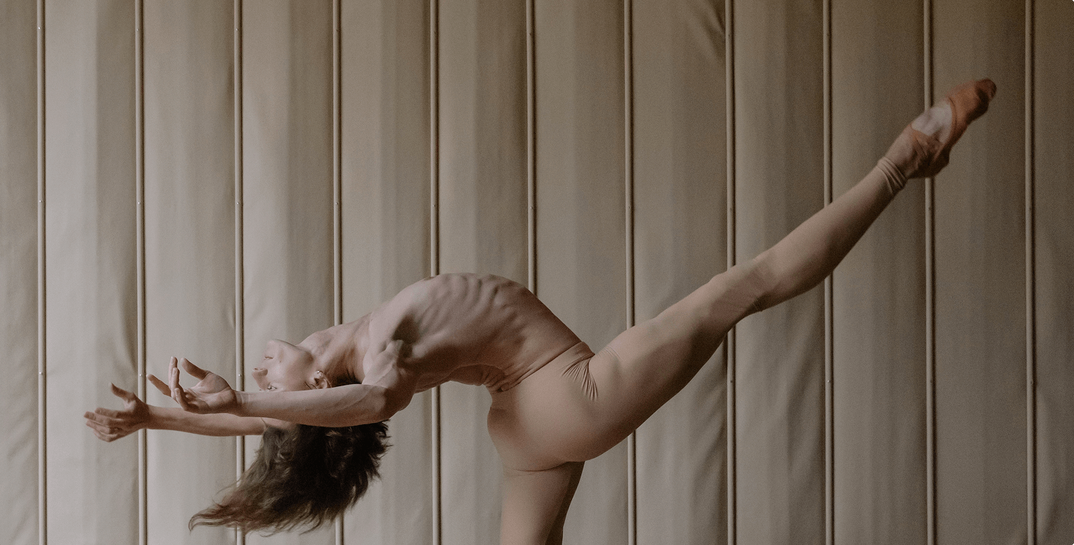 Ballet dancer performing an elegant arabesque pose against a softly lit padded wall.