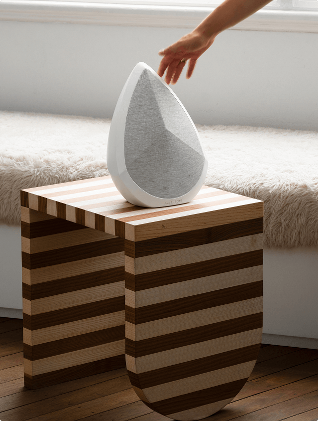 Pantheone Obsidian portable speaker on a side table and a hand reaching to touch it