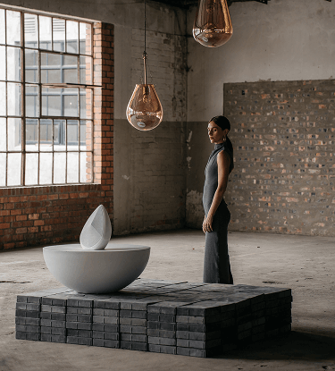 Woman in a minimalist loft standing beside a sculptural white Obsidian speaker.