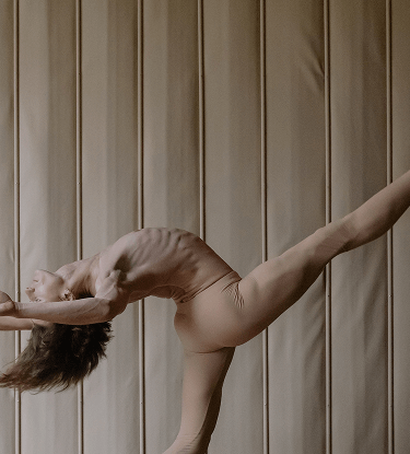 Ballet dancer performing an elegant arabesque pose against a softly lit padded wall.