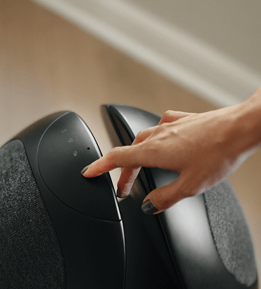 Hand gently touching the power button on a black Pantheone I 360 sound wireless speaker.
