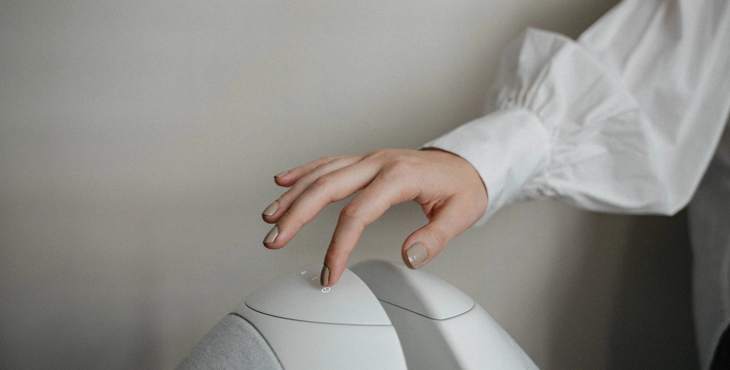 A close-up of a person's hand with silver nail polish hovering over the Pantheone I wireless speaker,  against a neutral gray background.