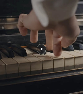Close-up of a hand playing a piano with a play button overlay