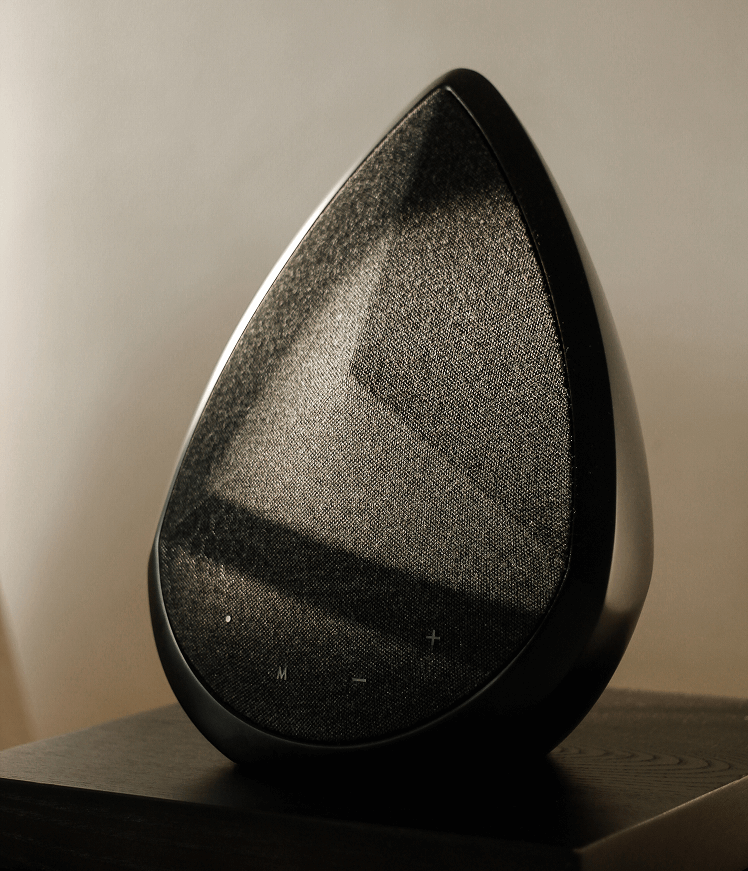 A black, teardrop-shaped Pantheone Obsidian speaker sits on a dark wooden bedside table