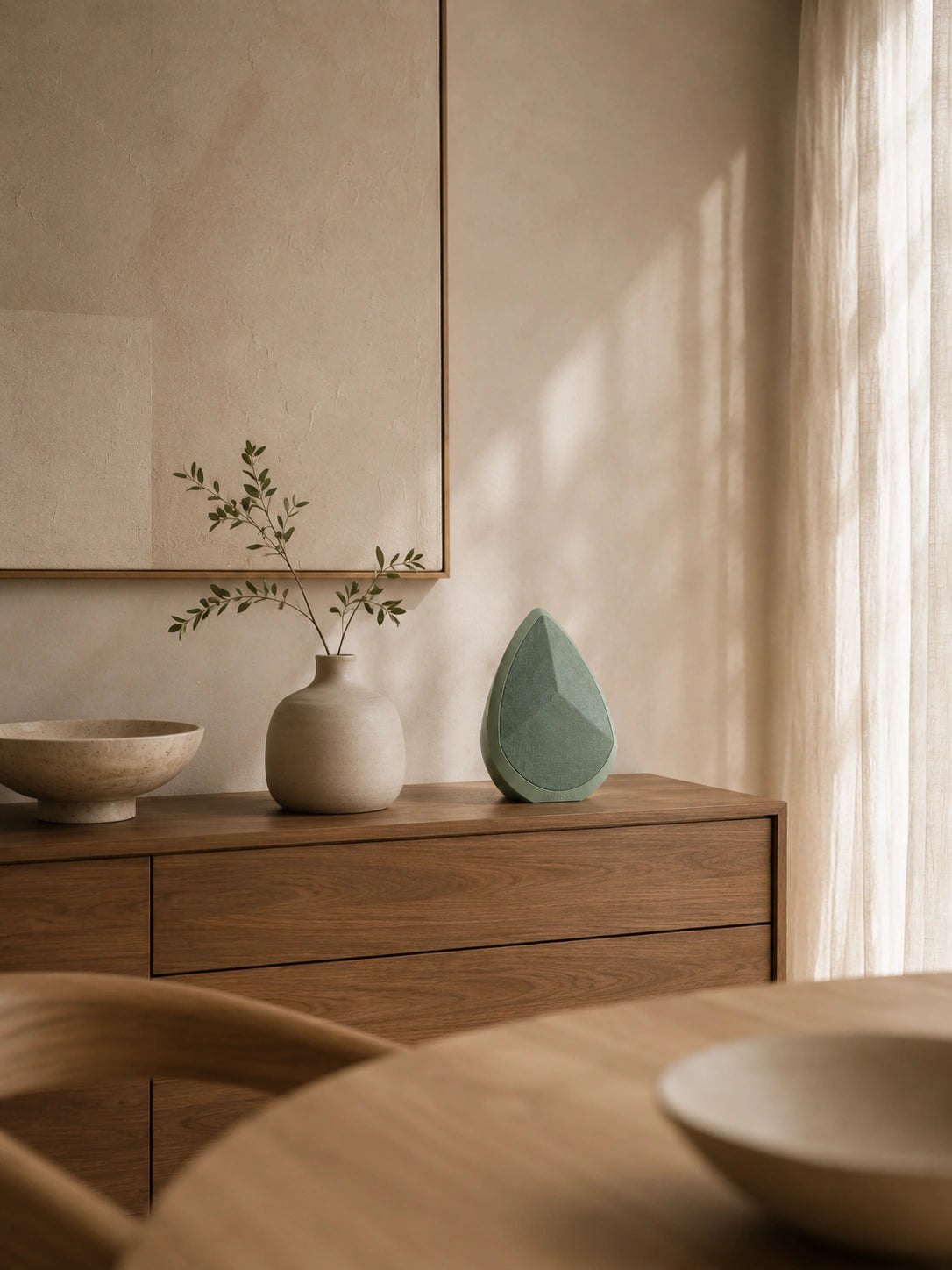 Wooden dresser with ceramic vases and a green sculpture in a softly lit room.