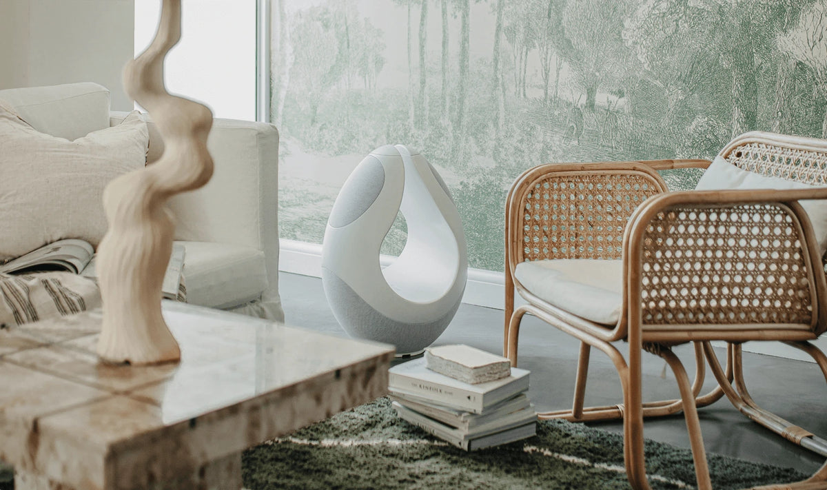 White Pantheone I high-end wireless speaker in modern luxury interior beside tufted ottoman and soft lounge seating